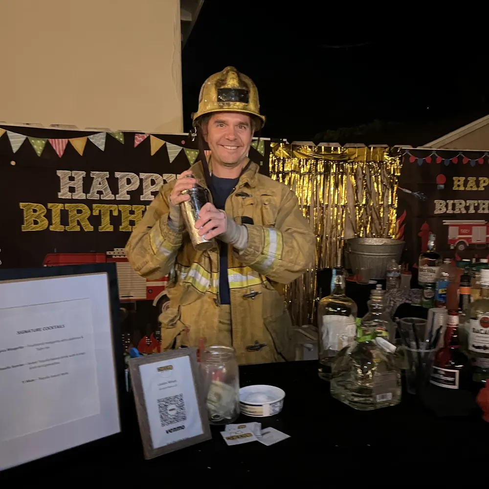 Justin in a firefighter costume holding a cocktail shaker at a fire truck themed birthday party bar