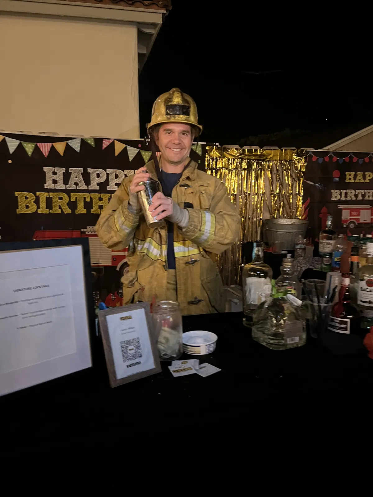 Justin in a firefighter costume holding a cocktail shaker at a fire truck themed birthday party bar