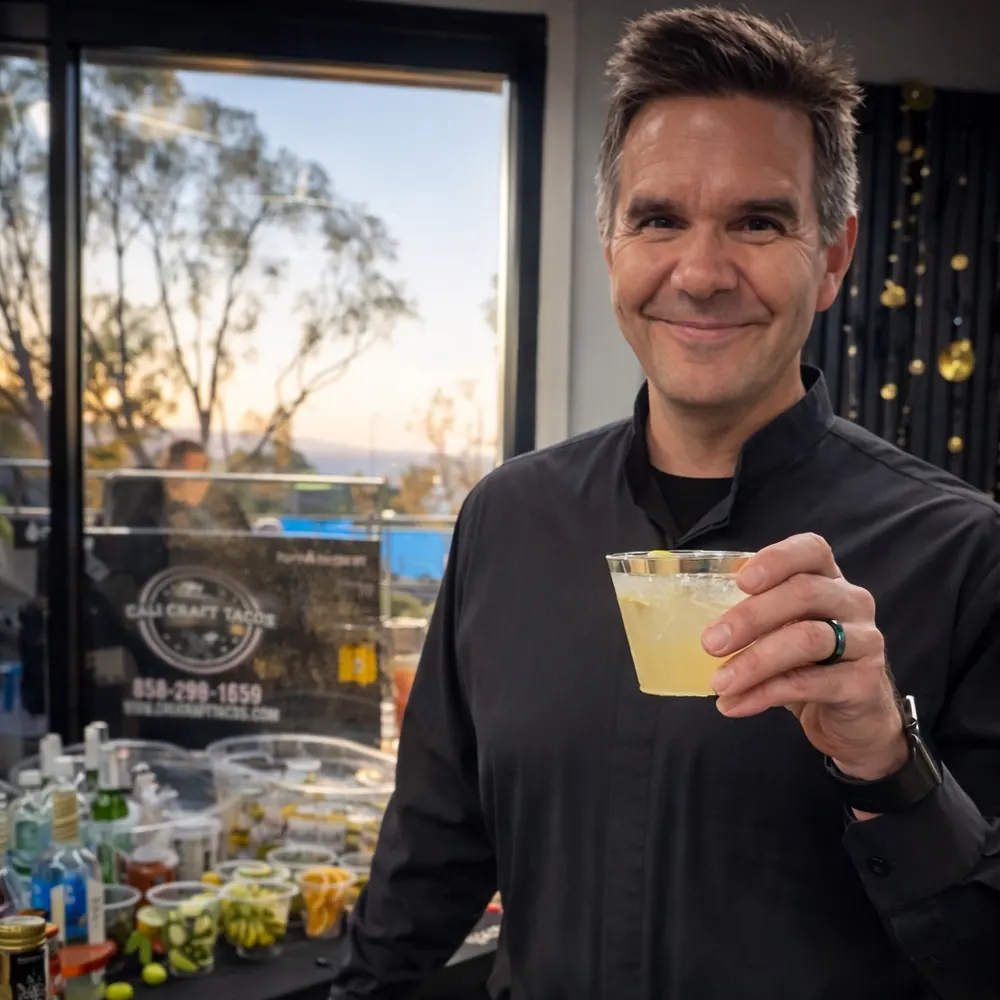 Justin in a black bartender shirt raising a cocktail at an evening event bar