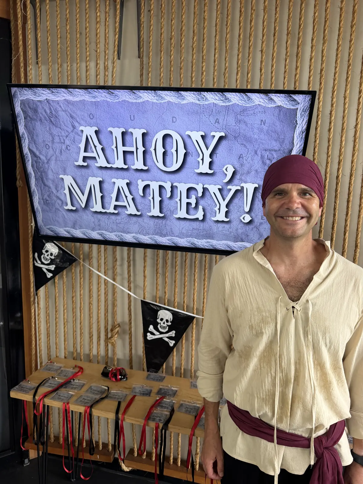 Justin dressed as a pirate beside an Ahoy Matey sign at a pirate themed party