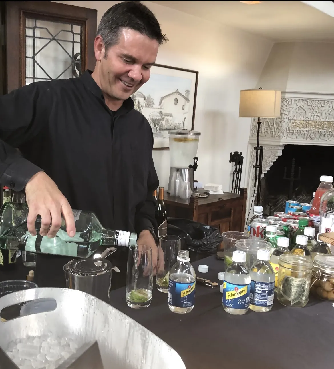 Justin pouring a clear spirit into a glass with lime at an indoor event bar lined with mixers