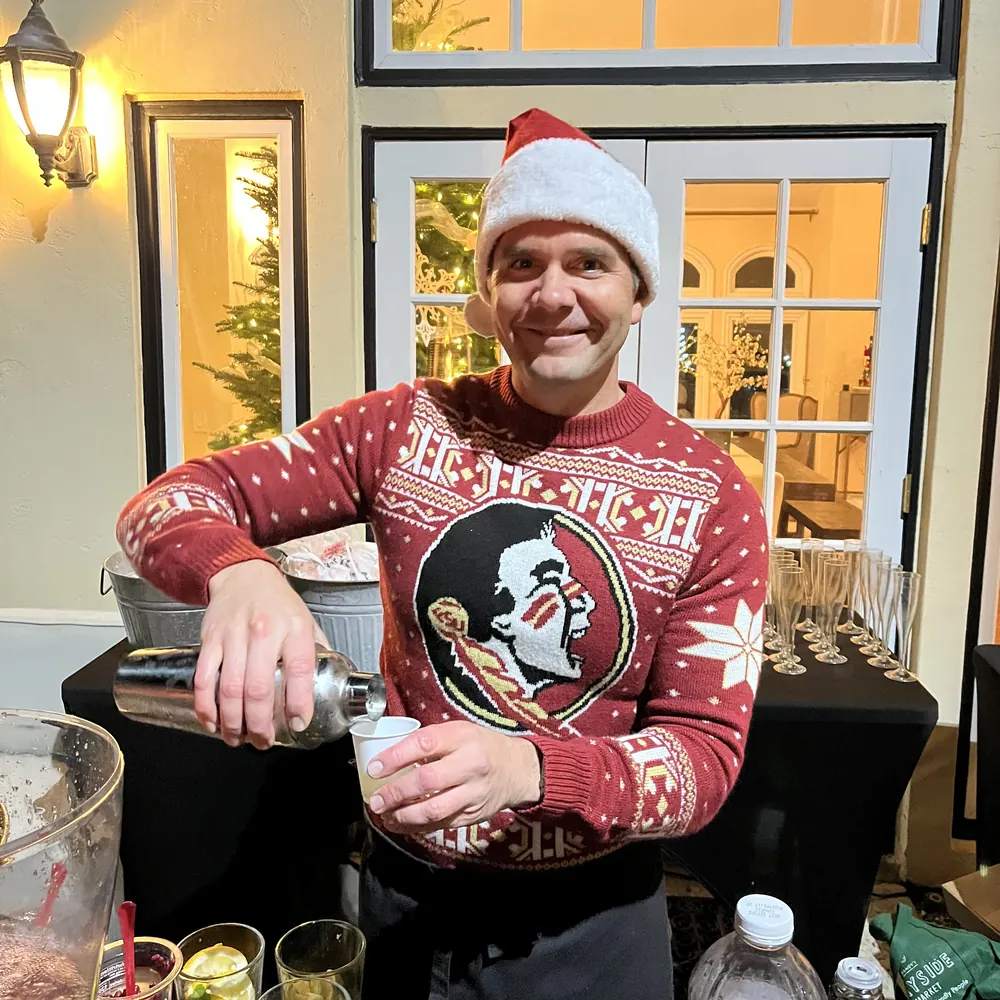 Justin in a Santa hat and holiday sweater pouring from a cocktail shaker at a holiday party bar