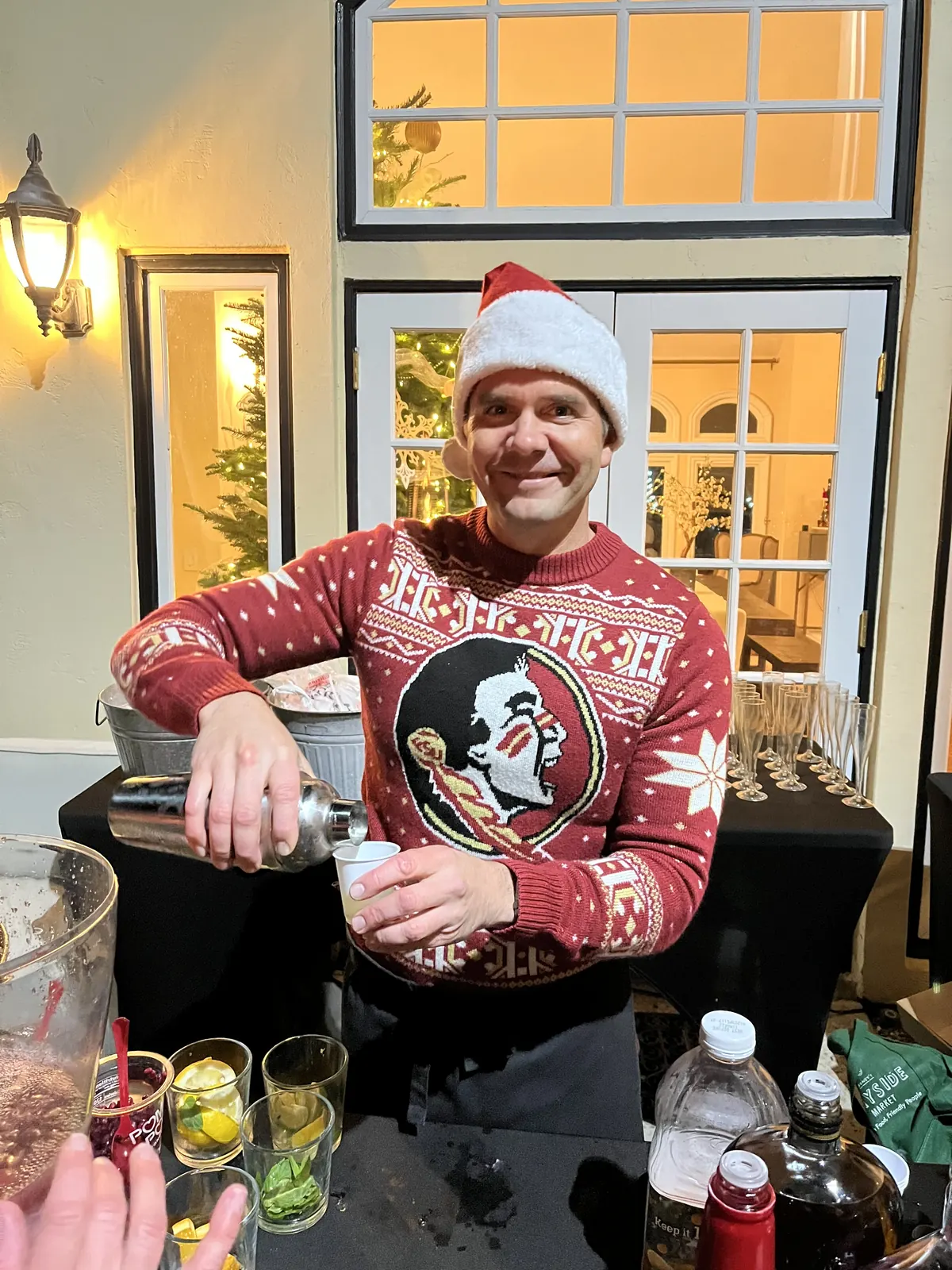 Justin in a Santa hat and holiday sweater pouring from a cocktail shaker at a holiday party bar