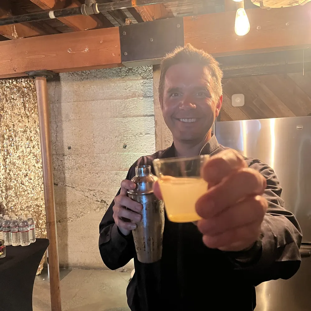 Justin holding a cocktail shaker and offering a freshly shaken drink