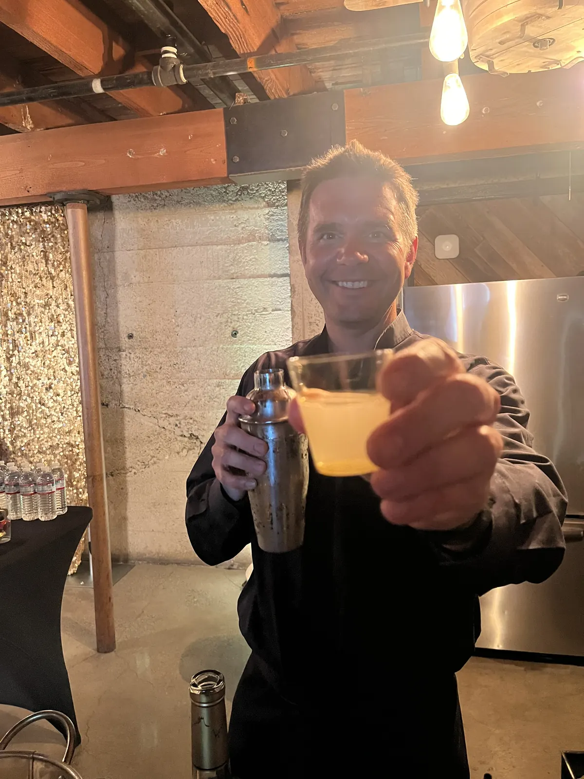 Justin holding a cocktail shaker and offering a freshly shaken drink