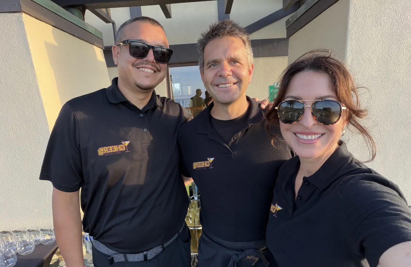 Three Cheers San Diego bartenders in branded polos smiling together at an outdoor event