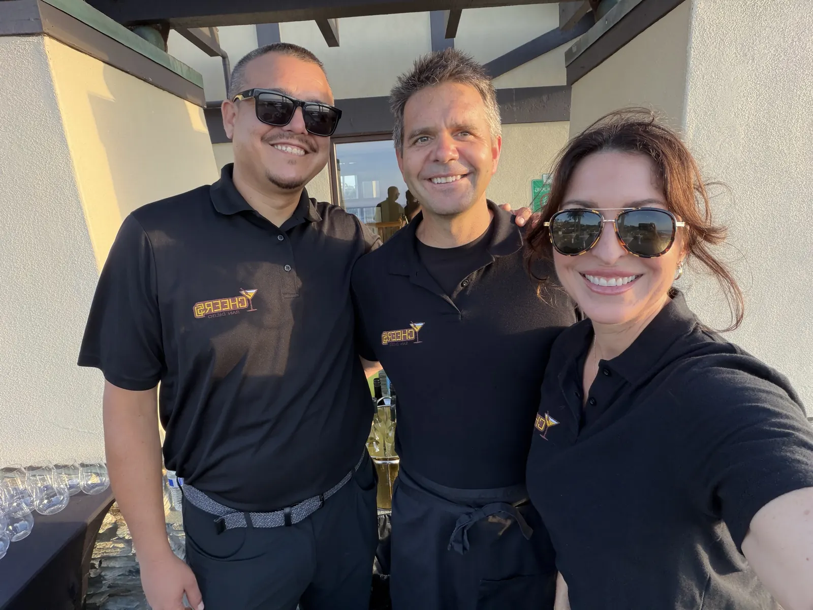 Three Cheers San Diego bartenders in branded polos smiling together at an outdoor event