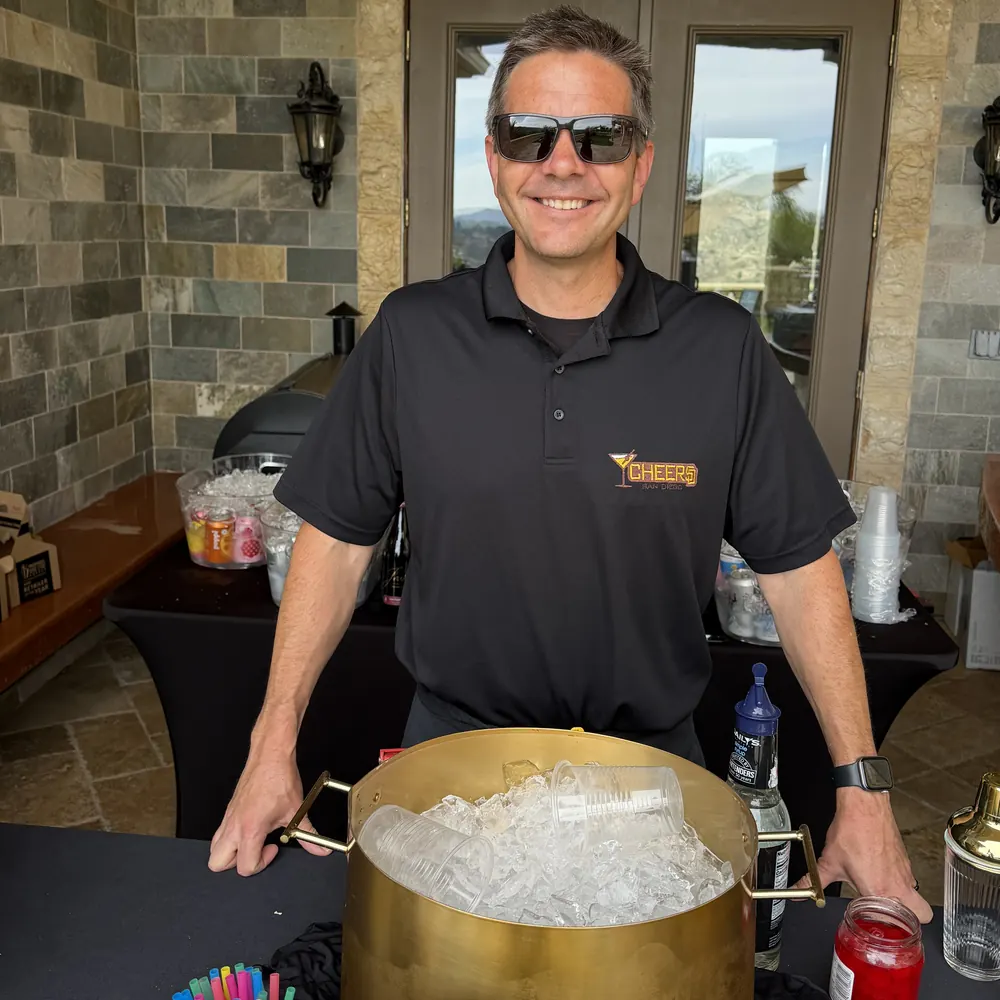 Justin in a Cheers San Diego polo behind a gold ice tub at a covered patio bar