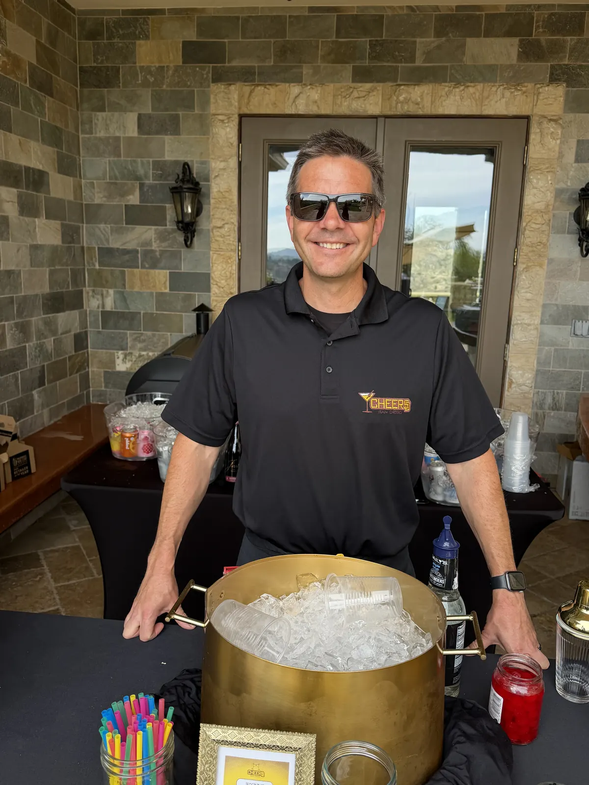 Justin in a Cheers San Diego polo behind a gold ice tub at a covered patio bar