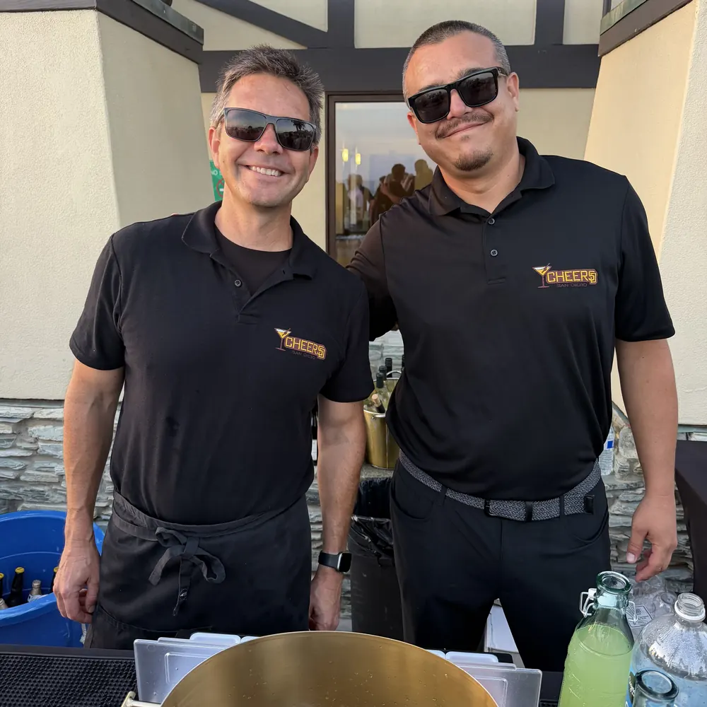 Two Cheers San Diego bartenders in branded polos behind an event bar with a gold ice tub