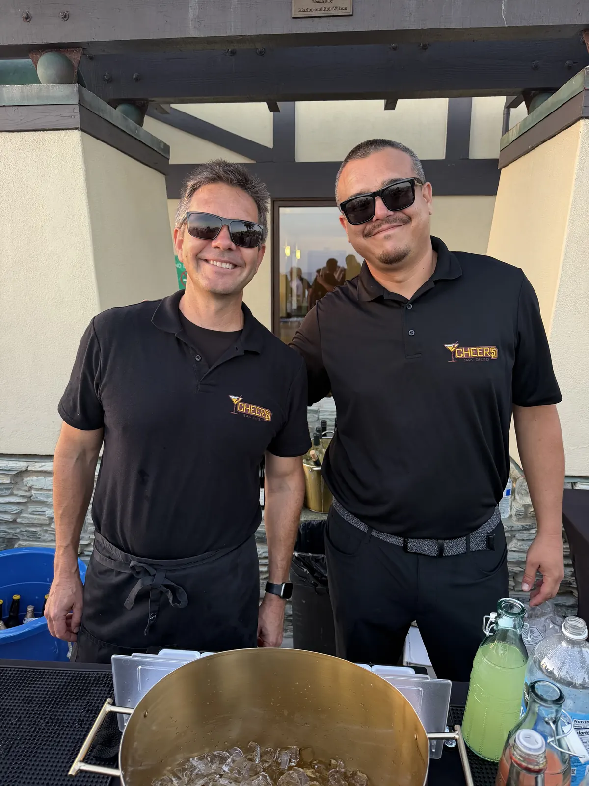 Two Cheers San Diego bartenders in branded polos behind an event bar with a gold ice tub